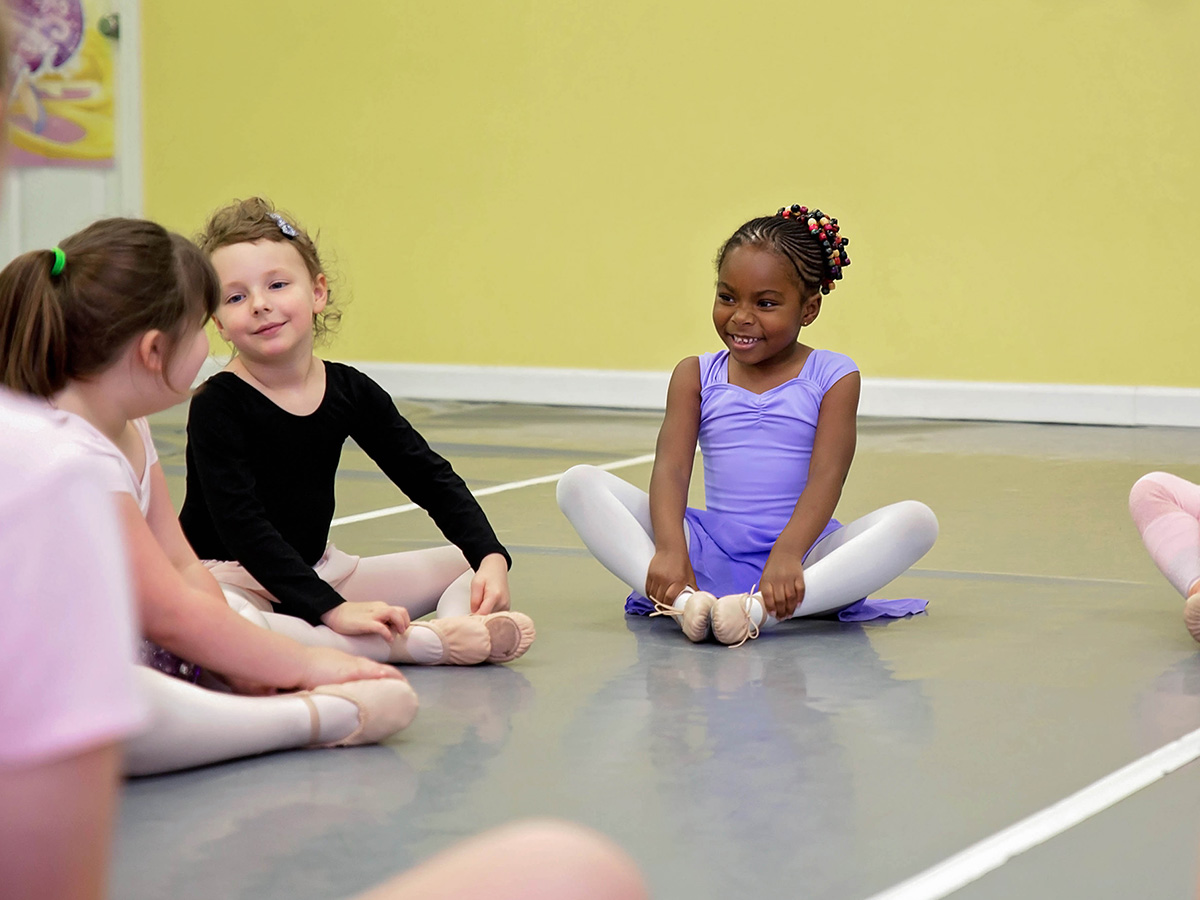 group of young ballerinas smiling and stretching in circle on the dance studio floor