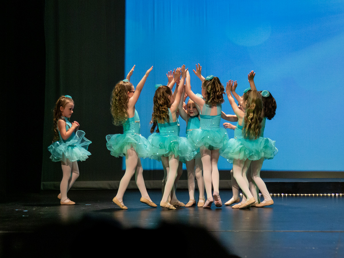 group of young dancers give each other high fives on stage following dance performance