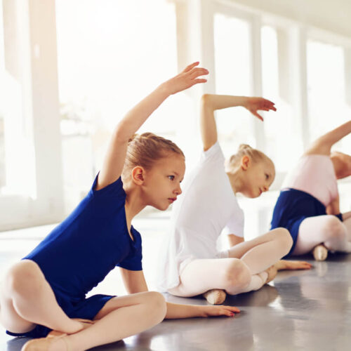 several ballet dancers stretching in a white room, wearing blue and white liatards,
