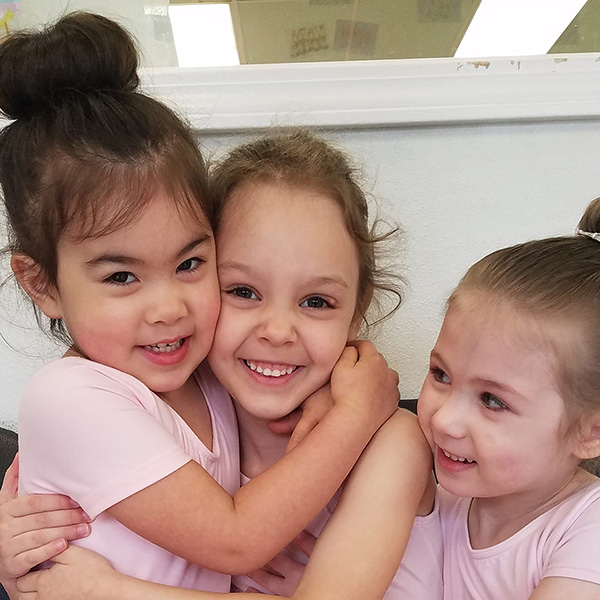 three little girls in dance uniforms smiling and hugging