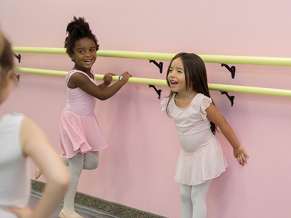 three young girls of various ethnicities smiling and laughing while dressed in tutus for dance class